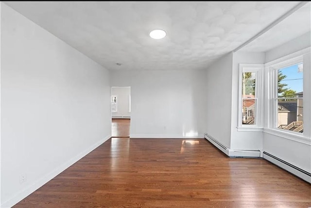 unfurnished room featuring baseboards, wood finished floors, and a baseboard radiator