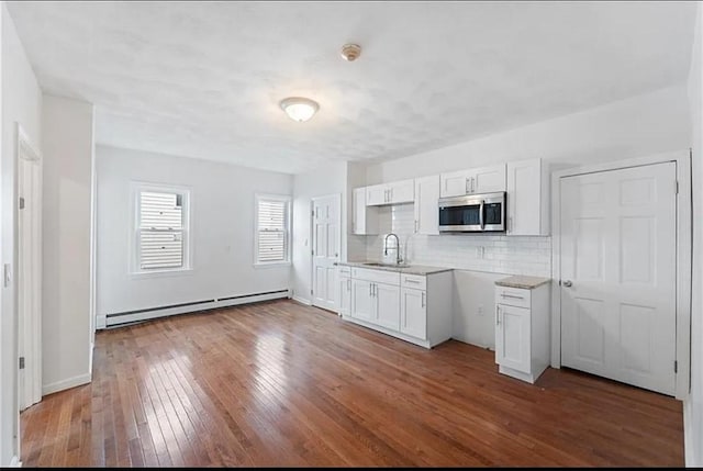 kitchen with a sink, a baseboard heating unit, wood-type flooring, stainless steel microwave, and white cabinetry