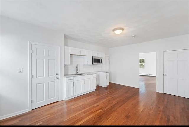 kitchen featuring white cabinets, dark wood-style floors, a sink, stainless steel microwave, and decorative backsplash