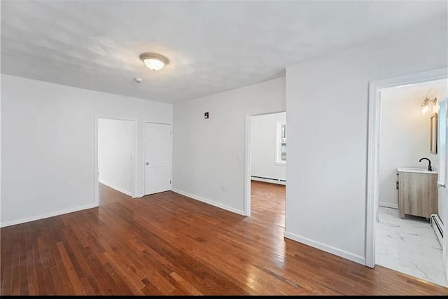 unfurnished room with baseboard heating, baseboards, wood finished floors, and a sink