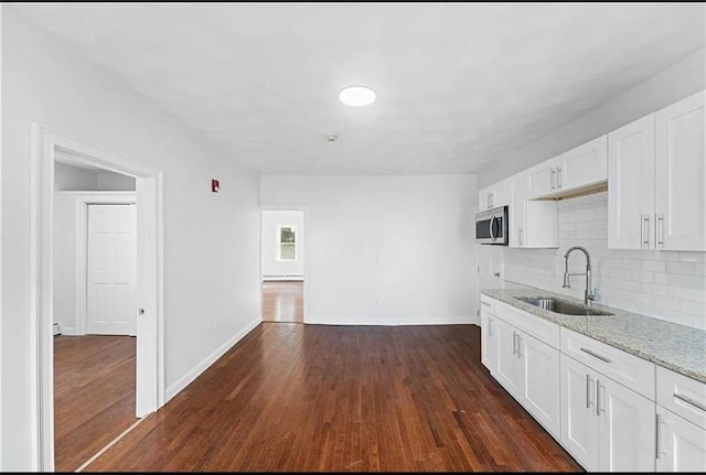 kitchen with a sink, stainless steel microwave, baseboards, decorative backsplash, and light stone countertops