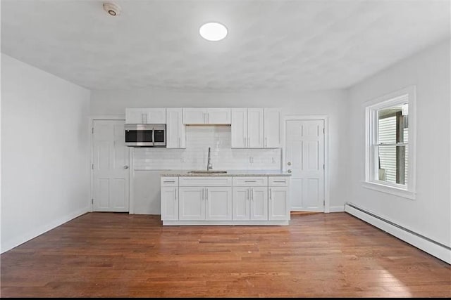 kitchen featuring a sink, stainless steel microwave, a baseboard heating unit, light wood-style flooring, and white cabinetry