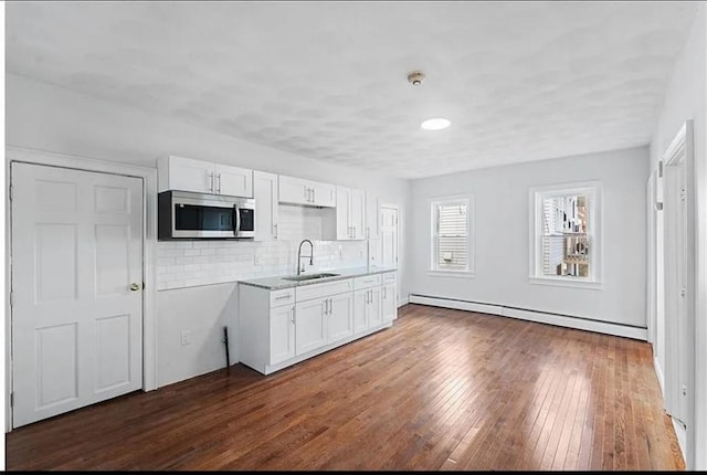 kitchen with white cabinets, dark wood-style floors, a sink, stainless steel microwave, and a baseboard radiator