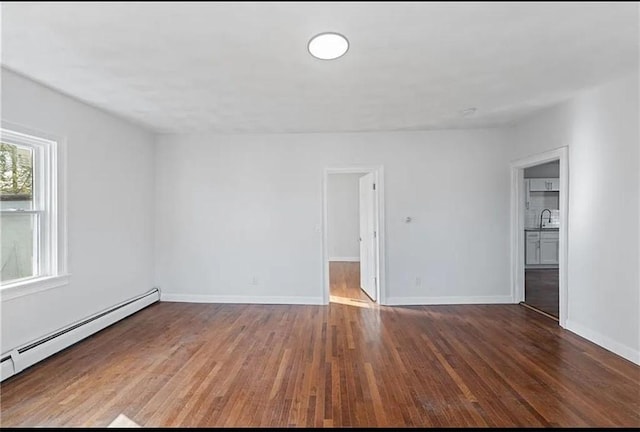 spare room featuring a baseboard heating unit, baseboards, wood finished floors, and a sink