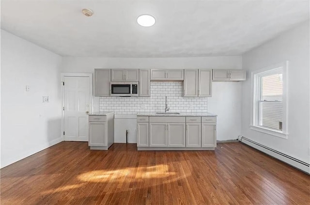 kitchen featuring a sink, stainless steel microwave, baseboard heating, wood finished floors, and gray cabinets