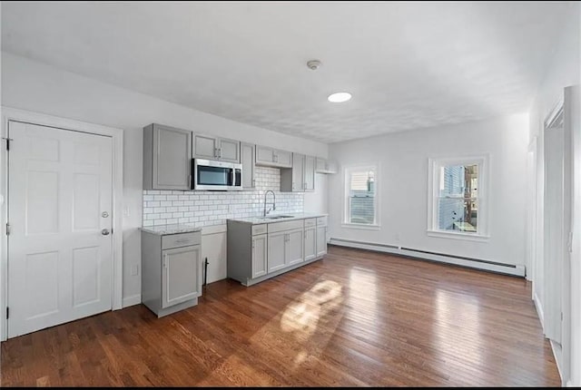 kitchen featuring a baseboard heating unit, stainless steel microwave, gray cabinets, and dark wood-style flooring