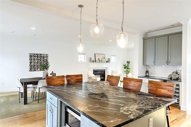 kitchen with tasteful backsplash, a sink, light wood finished floors, a glass covered fireplace, and ornamental molding