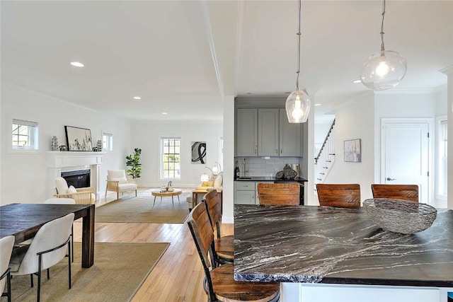 dining space featuring crown molding, stairs, a glass covered fireplace, recessed lighting, and light wood-style flooring