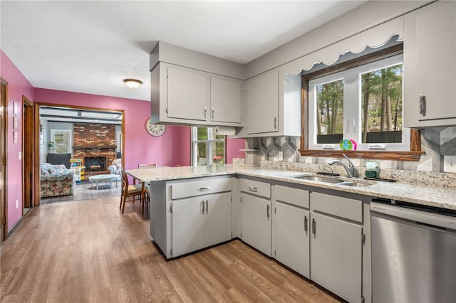 kitchen with tasteful backsplash, wood finished floors, a sink, dishwasher, and a peninsula