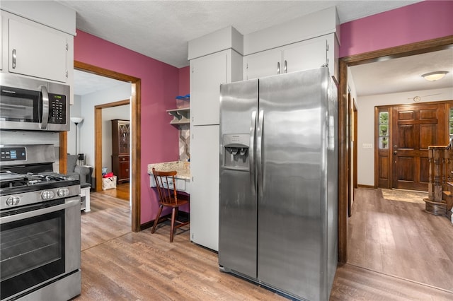 kitchen with stainless steel appliances, light countertops, baseboards, light wood-style flooring, and white cabinetry