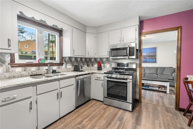 kitchen with white cabinets, backsplash, a sink, light wood-style floors, and appliances with stainless steel finishes