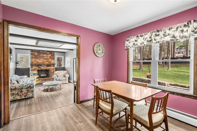 dining room featuring a baseboard heating unit, wood finished floors, a brick fireplace, and baseboards