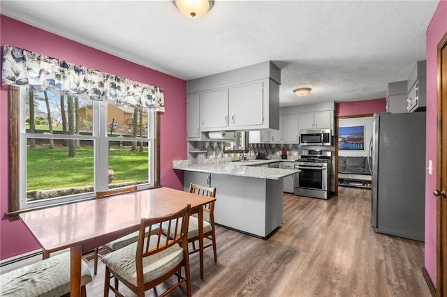 kitchen with white cabinets, a peninsula, wood finished floors, appliances with stainless steel finishes, and a baseboard radiator