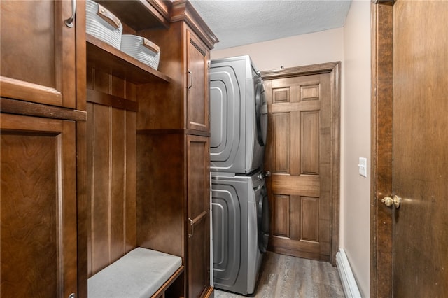 laundry area featuring wood finished floors, a textured ceiling, stacked washer / dryer, cabinet space, and baseboards
