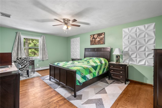 bedroom featuring baseboards, visible vents, baseboard heating, wood finished floors, and a ceiling fan