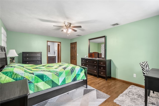bedroom featuring wood finished floors, visible vents, a ceiling fan, baseboards, and ensuite bathroom