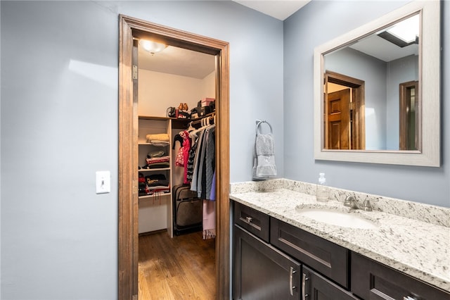 bathroom featuring wood finished floors, a spacious closet, and vanity
