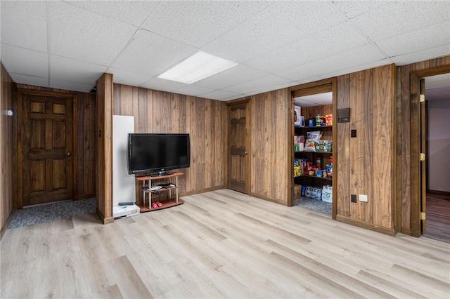 living room featuring light wood-style flooring, wood walls, baseboards, and a drop ceiling