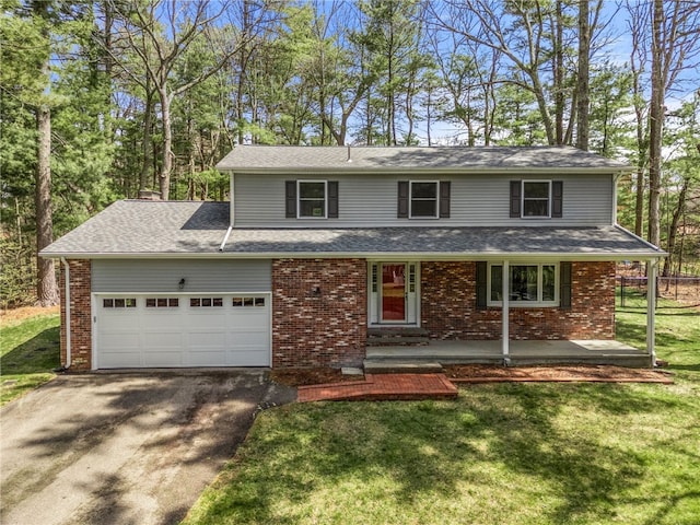 traditional-style house with a front yard, a garage, covered porch, aphalt driveway, and brick siding