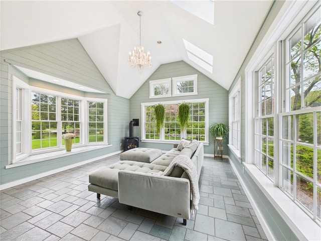 sunroom featuring lofted ceiling, a wood stove, a skylight, stone tile flooring, and a chandelier