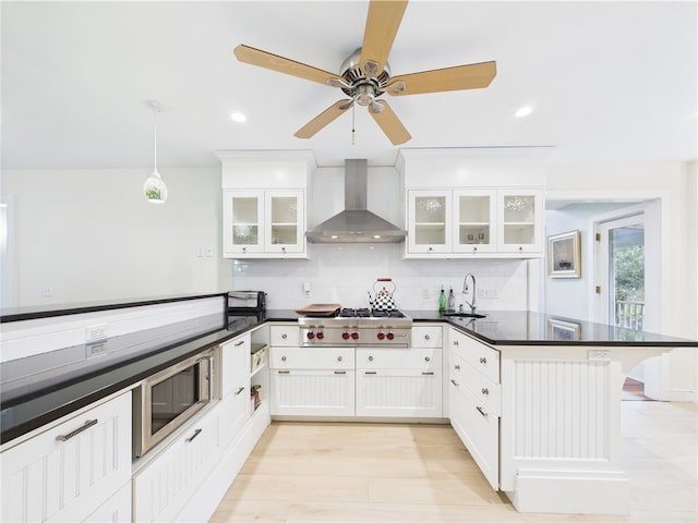 kitchen with wall chimney range hood, a peninsula, stainless steel gas stovetop, a sink, and dark countertops