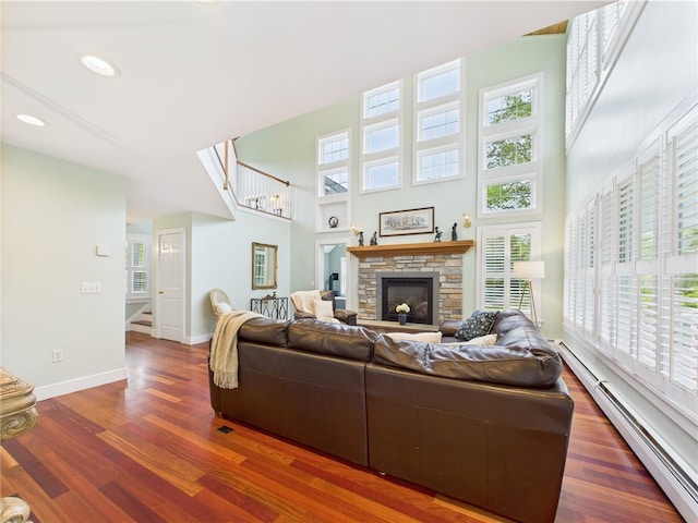 living area with baseboard heating, stairs, baseboards, wood finished floors, and a high ceiling