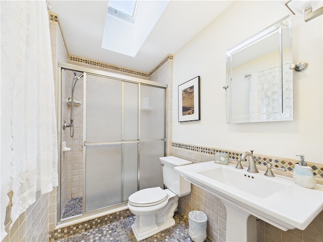 bathroom with a skylight, a stall shower, toilet, tile walls, and a sink