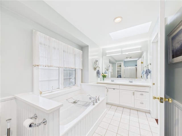 bathroom featuring a skylight, tile patterned floors, a garden tub, vanity, and a wainscoted wall