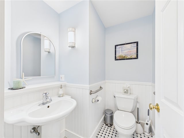 half bath featuring toilet, a wainscoted wall, tile patterned floors, and a sink