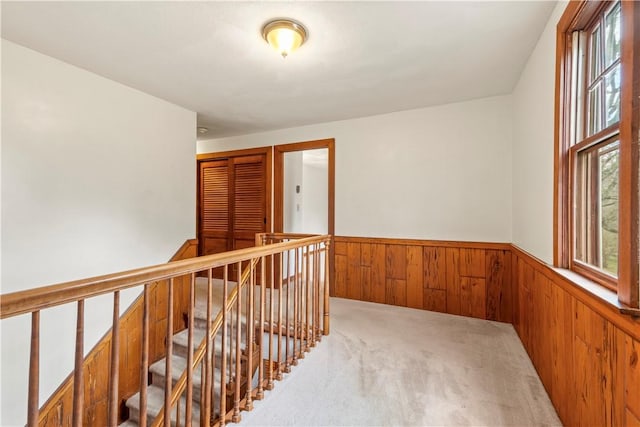 hallway featuring a wainscoted wall, light colored carpet, wood walls, and an upstairs landing