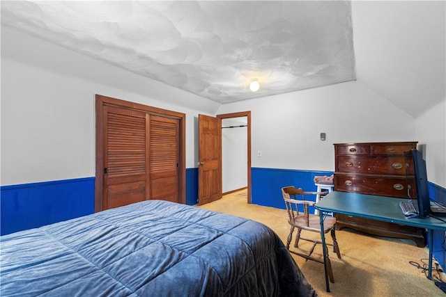 bedroom featuring lofted ceiling, a closet, light colored carpet, and wainscoting