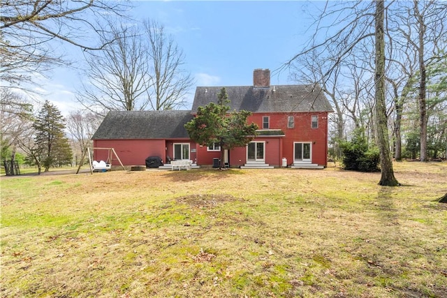 rear view of house with entry steps, a lawn, and a chimney