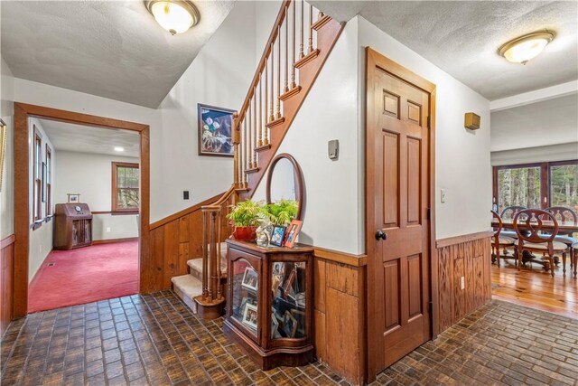 interior space with brick patterned floor, wood walls, stairs, and wainscoting
