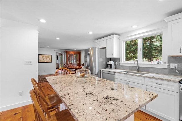 kitchen with light stone counters, a sink, white cabinets, appliances with stainless steel finishes, and a kitchen island