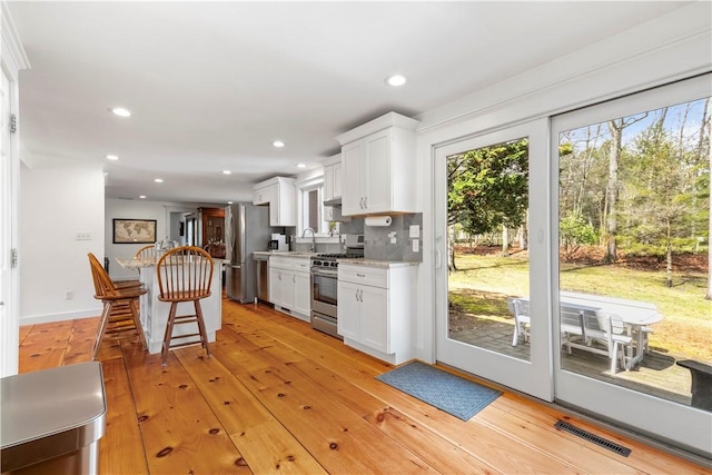 kitchen with white cabinets, stainless steel appliances, a kitchen breakfast bar, and visible vents