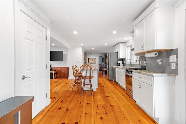 kitchen with a kitchen breakfast bar, a sink, light wood-style floors, appliances with stainless steel finishes, and white cabinetry