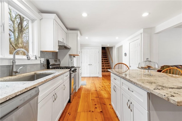 kitchen with white cabinets, recessed lighting, under cabinet range hood, a sink, and appliances with stainless steel finishes