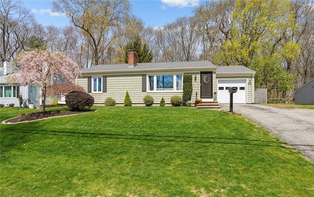 single story home featuring a chimney, an attached garage, driveway, and a front yard