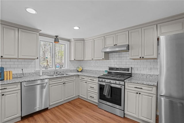 kitchen featuring a sink, light wood-type flooring, appliances with stainless steel finishes, backsplash, and under cabinet range hood