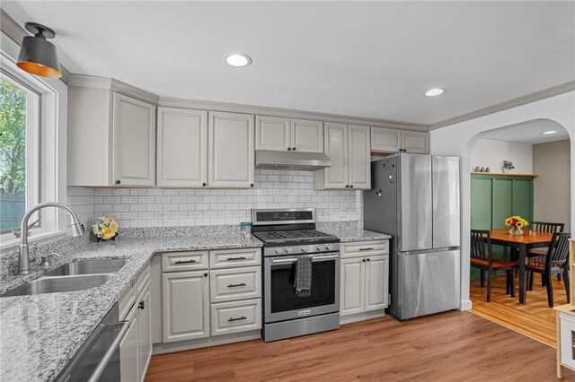 kitchen featuring arched walkways, a sink, tasteful backsplash, under cabinet range hood, and appliances with stainless steel finishes