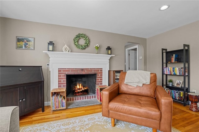 sitting room featuring recessed lighting, arched walkways, a brick fireplace, and light wood-style flooring
