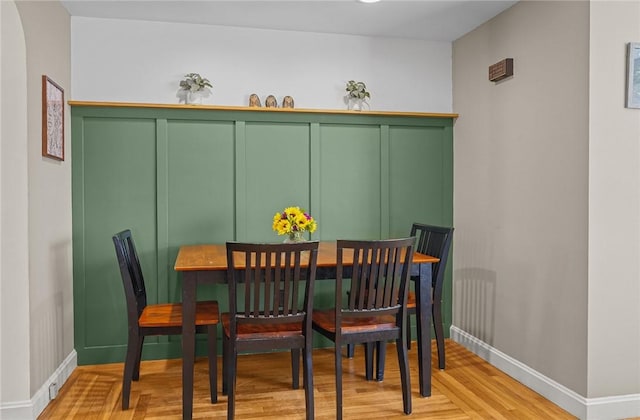 dining room featuring baseboards, wood finished floors, and a decorative wall
