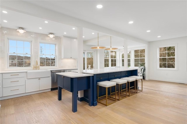 kitchen featuring light wood finished floors, white cabinets, a sink, dishwasher, and a kitchen island