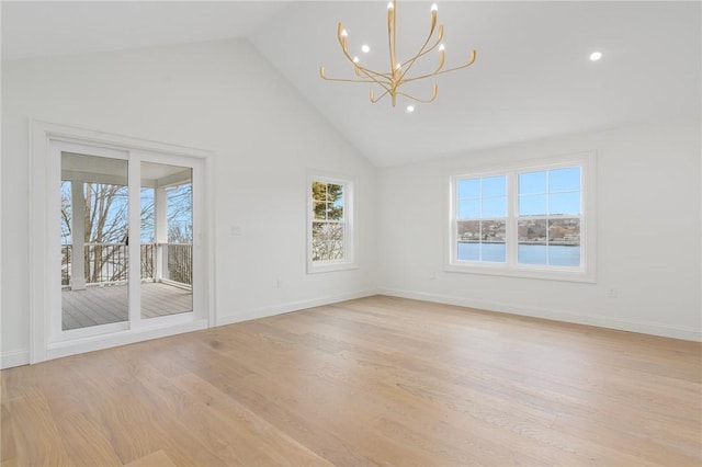 spare room with a chandelier, light wood-style floors, a wealth of natural light, and high vaulted ceiling