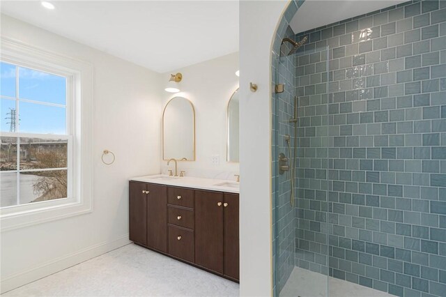 full bathroom with baseboards, a sink, double vanity, and a tile shower