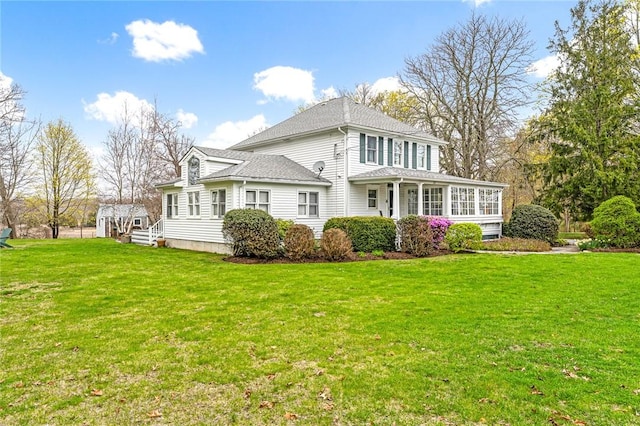rear view of property with a lawn, roof with shingles, and a sunroom