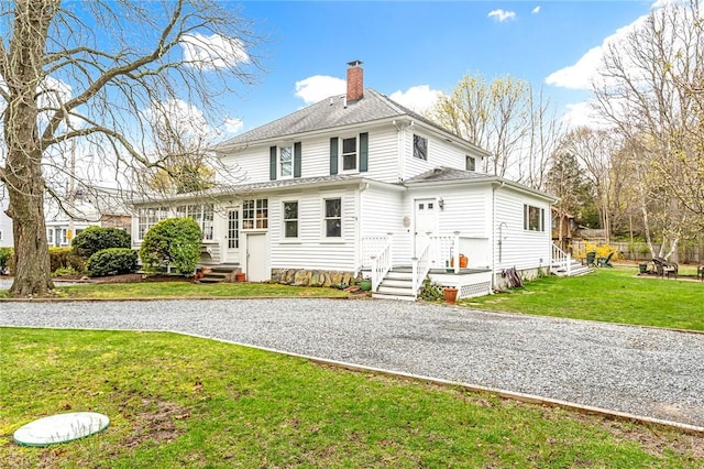 rear view of property with roof with shingles, a chimney, and a lawn