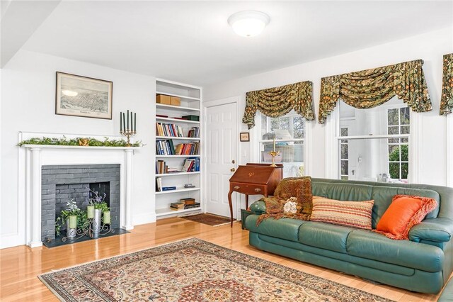 living room featuring a fireplace with flush hearth, built in shelves, and wood finished floors