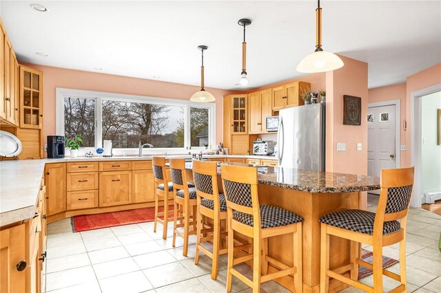 kitchen featuring light tile patterned floors, glass insert cabinets, freestanding refrigerator, and a breakfast bar area
