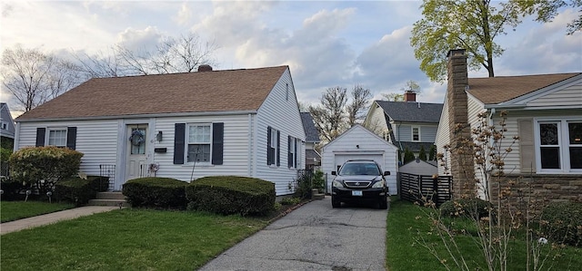 view of front facade featuring driveway, a chimney, a front yard, an outbuilding, and a detached garage